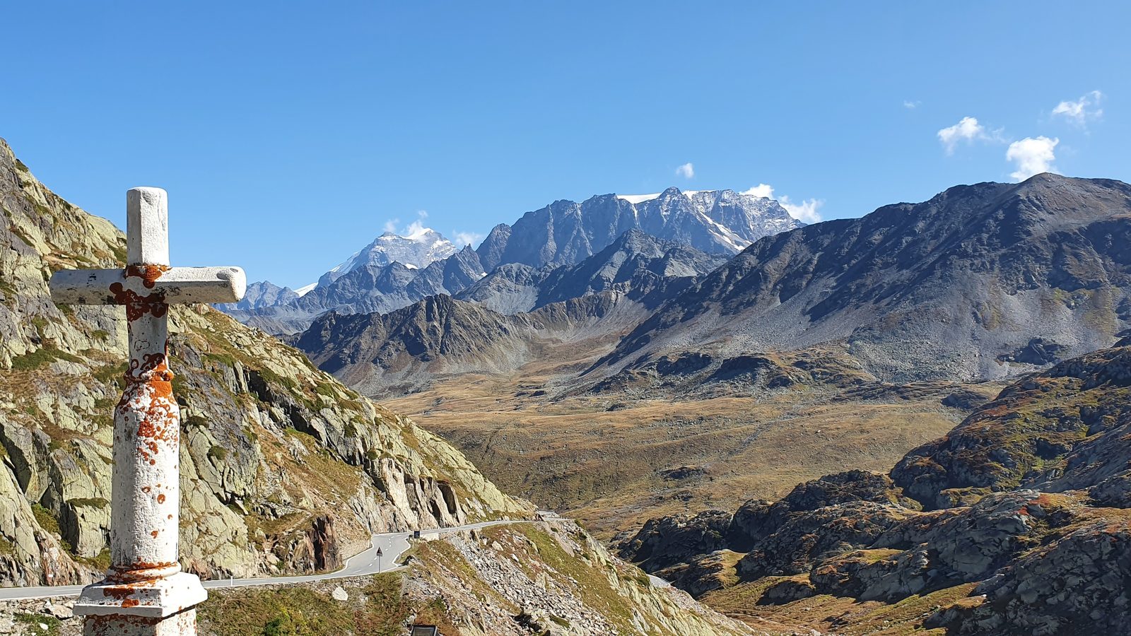 A stone cross above the hairpins of the Great St Bernard pass road, with bare rock and snow-capped peaks beyond