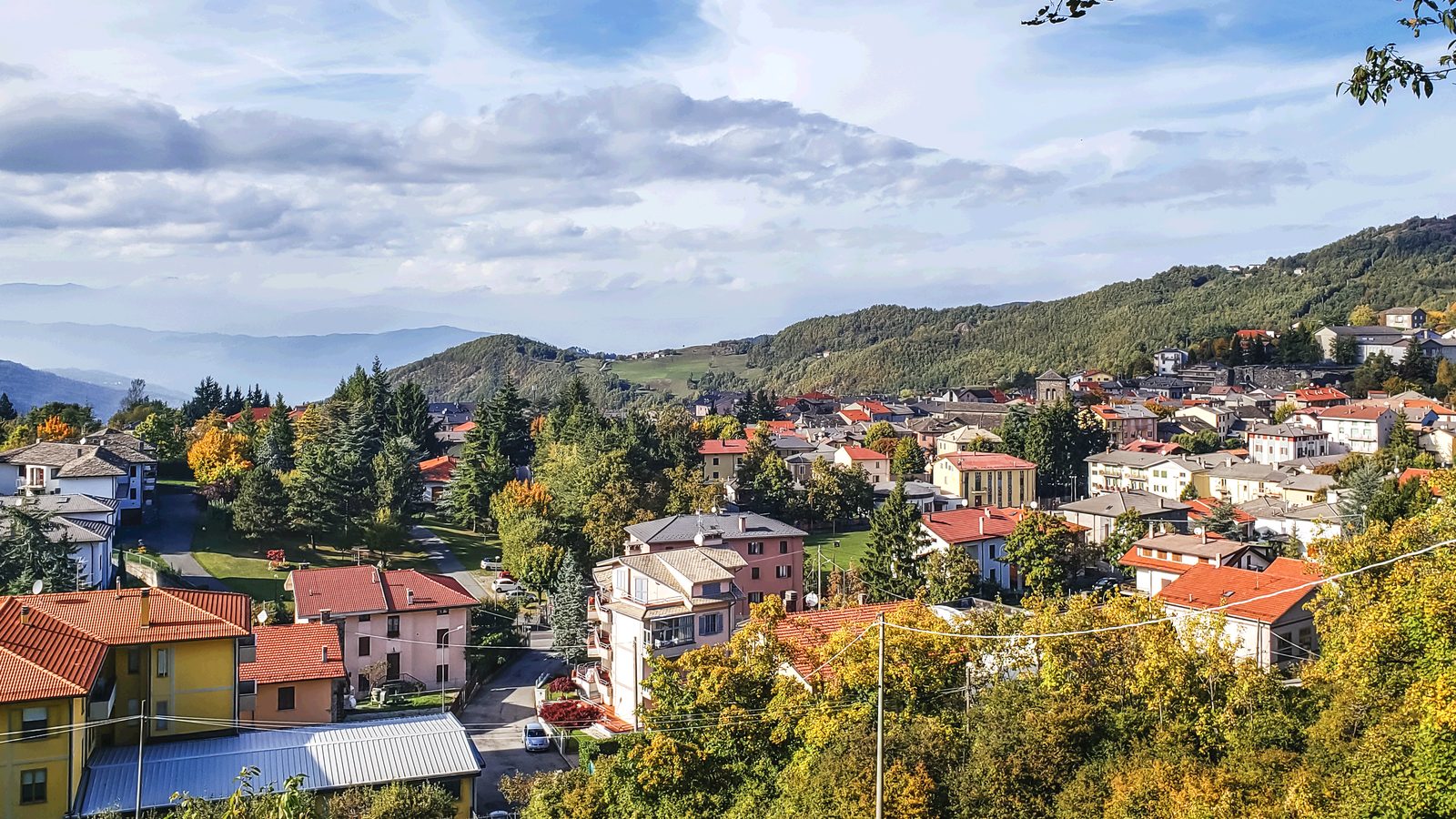 Red-roofed houses of an Apennine hill town among autumn trees, on the Fornovo di Taro to Berceto stage