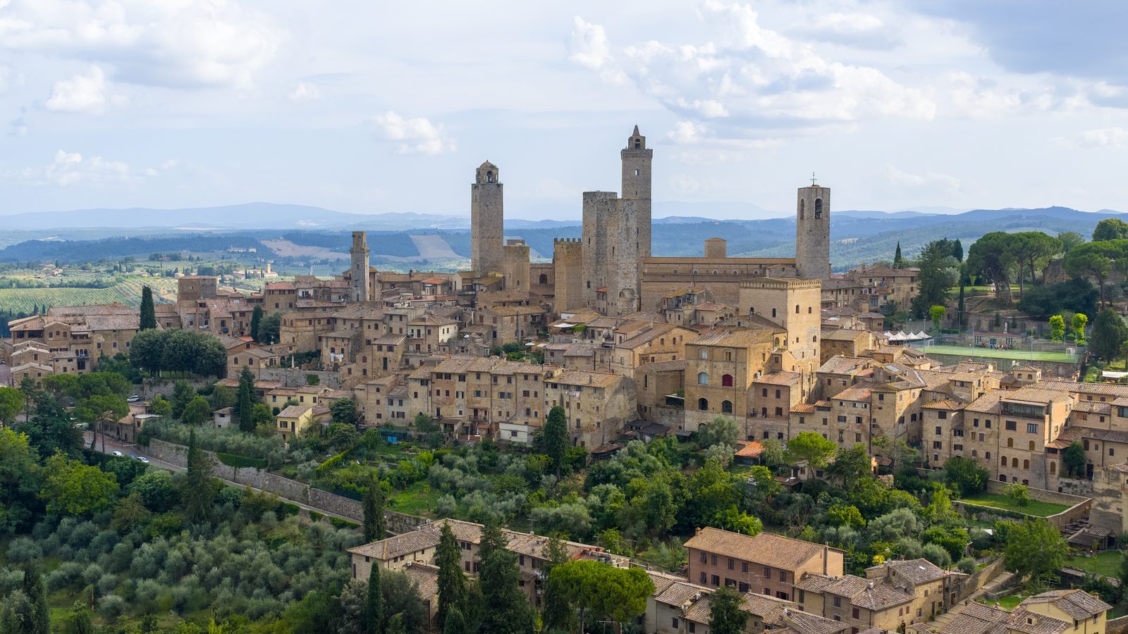 The medieval stone towers of San Gimignano rising above its rooftops, with Tuscan hills behind
