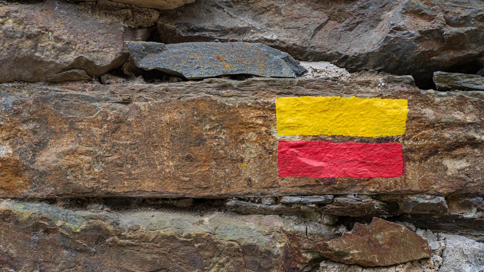 Painted yellow and red waymark flashes on a dry-stone wall beside a footpath